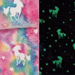 Wellness Fleece Glow In The Dark Eenhoorn stof met witte eenhoorns en sterren op een regenboogkleurige achtergrond. Een droom voor unicorn-fans