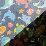 Wellness Fleece Glow In The Dark Zeedieren stof met walvissen, zeepaardjes, schildpadden en kleurrijke oceaanelementen.