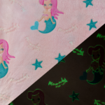 Wellness Fleece Glow In The Dark Zeemeerminnen stof met roze achtergrond, turquoise sterren en de tekst “Mermaids are real